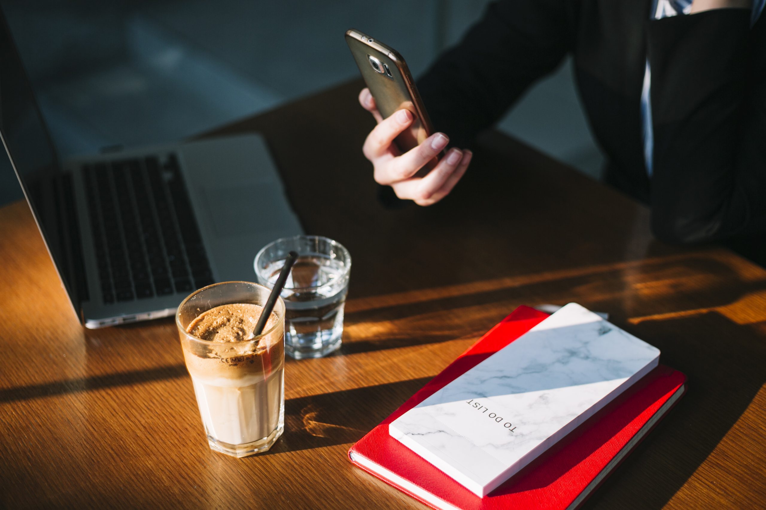 businesswoman-s-hand-using-cellphone-with-laptop-chocolate-milkshake-books-wooden-desk-scaled.jpg